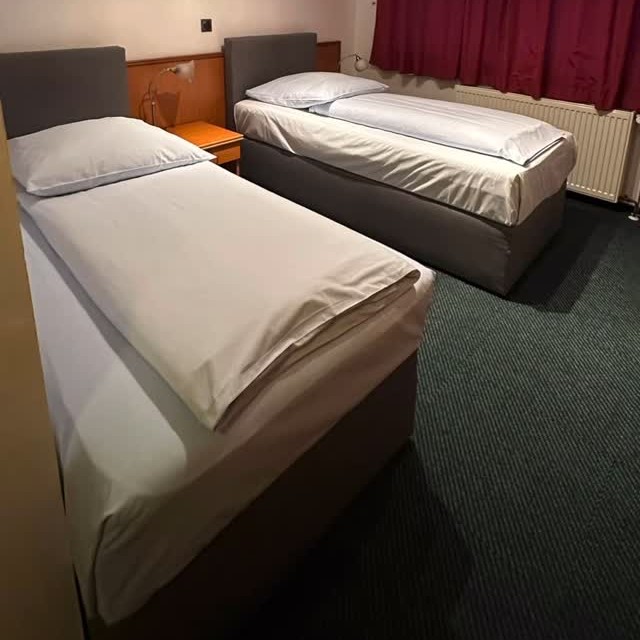 Zimmer im Hotel Nike mit zwei frisch bezogenen Einzelbetten und bordeauxroten Vorhängen